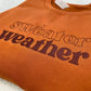 Ginger sweatshirt with 'sweater weather' text on a textured surface