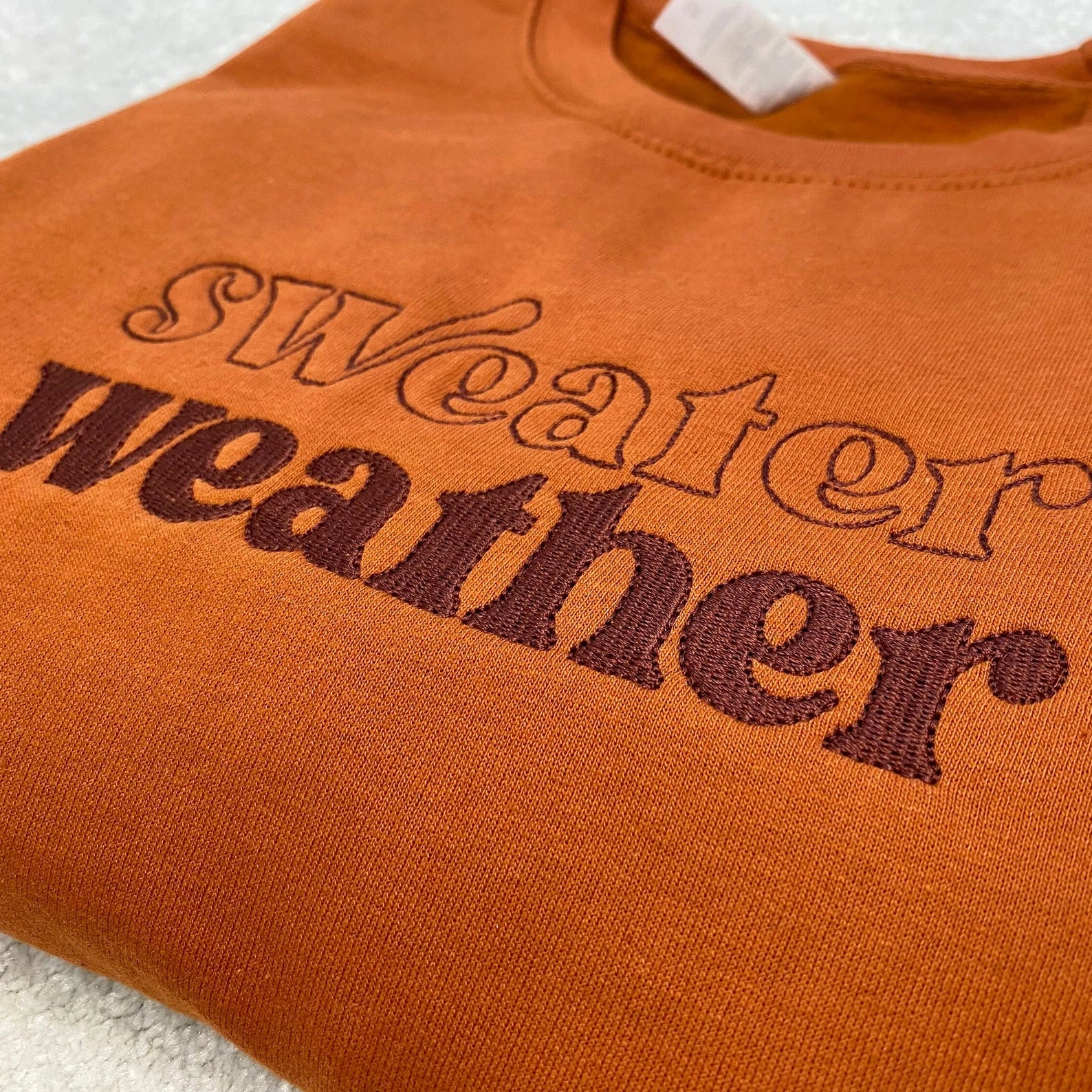 Ginger sweatshirt with 'sweater weather' text on a textured surface