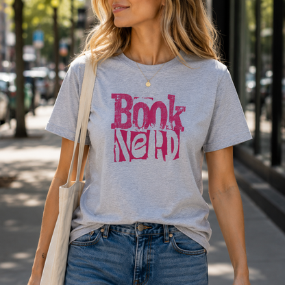 A woman wearing a light heather gray graphic t-shirt with a pink 'Book Nerd' print, styled with blue jeans and a cream canvas tote bag, walking on a sunny city street.