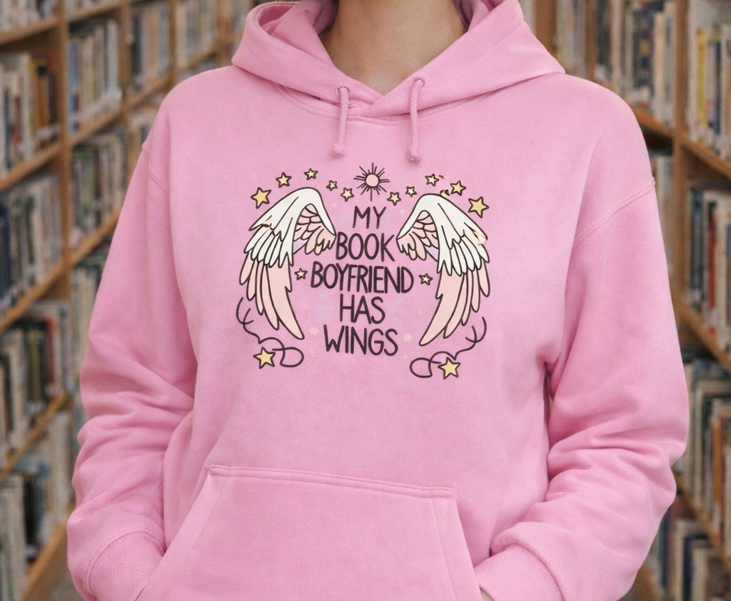 Person wearing a pink hoodie with 'My book boyfriend has wings' design in a library setting