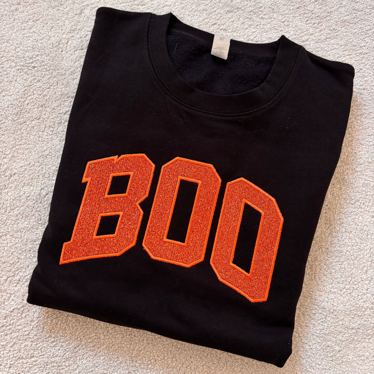 Black sweatshirt folded with large BOO in orange glitter applique.