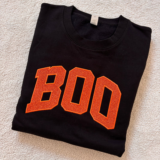 Black sweatshirt folded with large BOO in orange glitter applique.