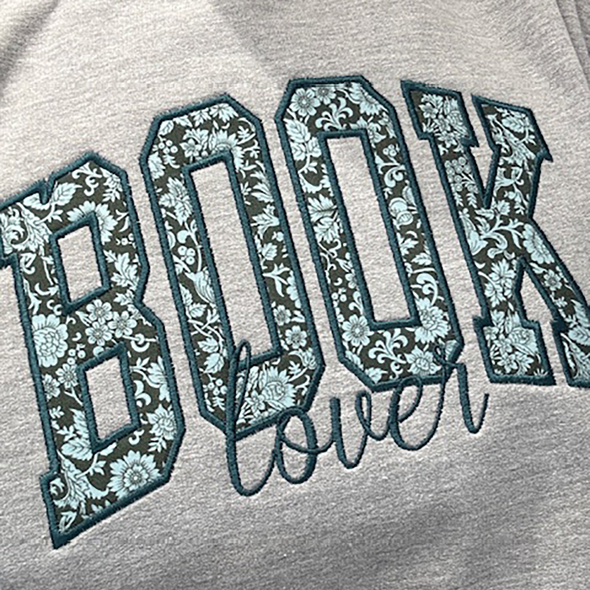 BOOK embroidered using Liberty floral fabric and appliqued onto a grey sweatshirt. The word Lover embroidered underneath.