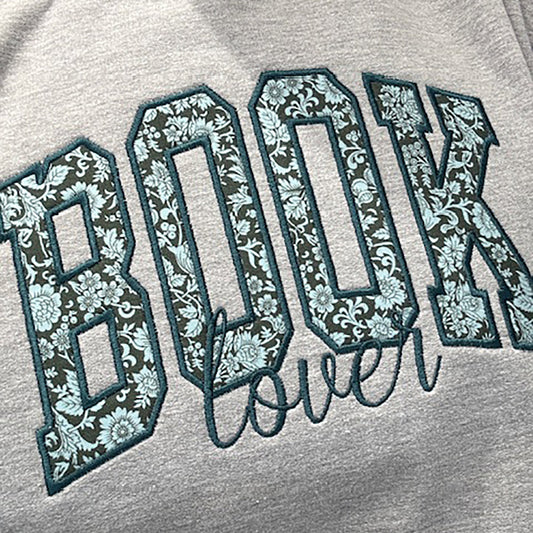 BOOK embroidered using Liberty floral fabric and appliqued onto a grey sweatshirt. The word Lover embroidered underneath.