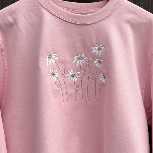 Pink sweatshirt with embroidered daisy flowers on a plain background