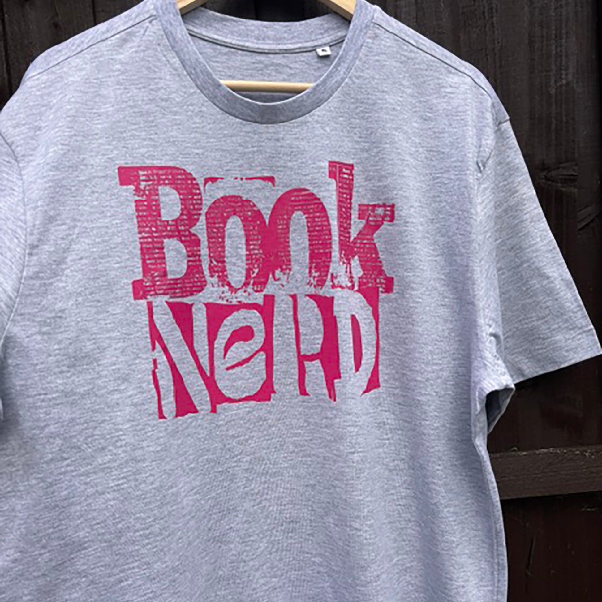 Grey t-shirt with 'Book Nerd' text in pink on a wooden hanger.