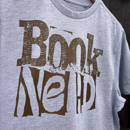 Grey t-shirt with 'Book Nerd' text in brown against a wooden background