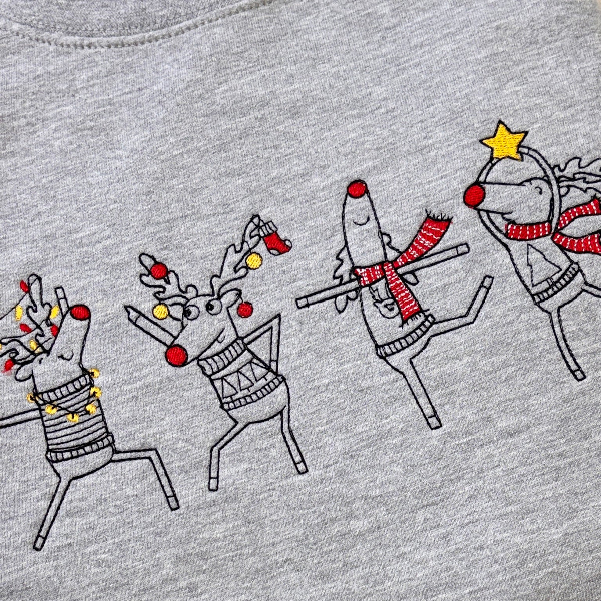 Close-up of a heather gray t-shirt featuring a graphic print of four dancing reindeer wearing holiday sweaters, scarves, red noses, and festive accessories.