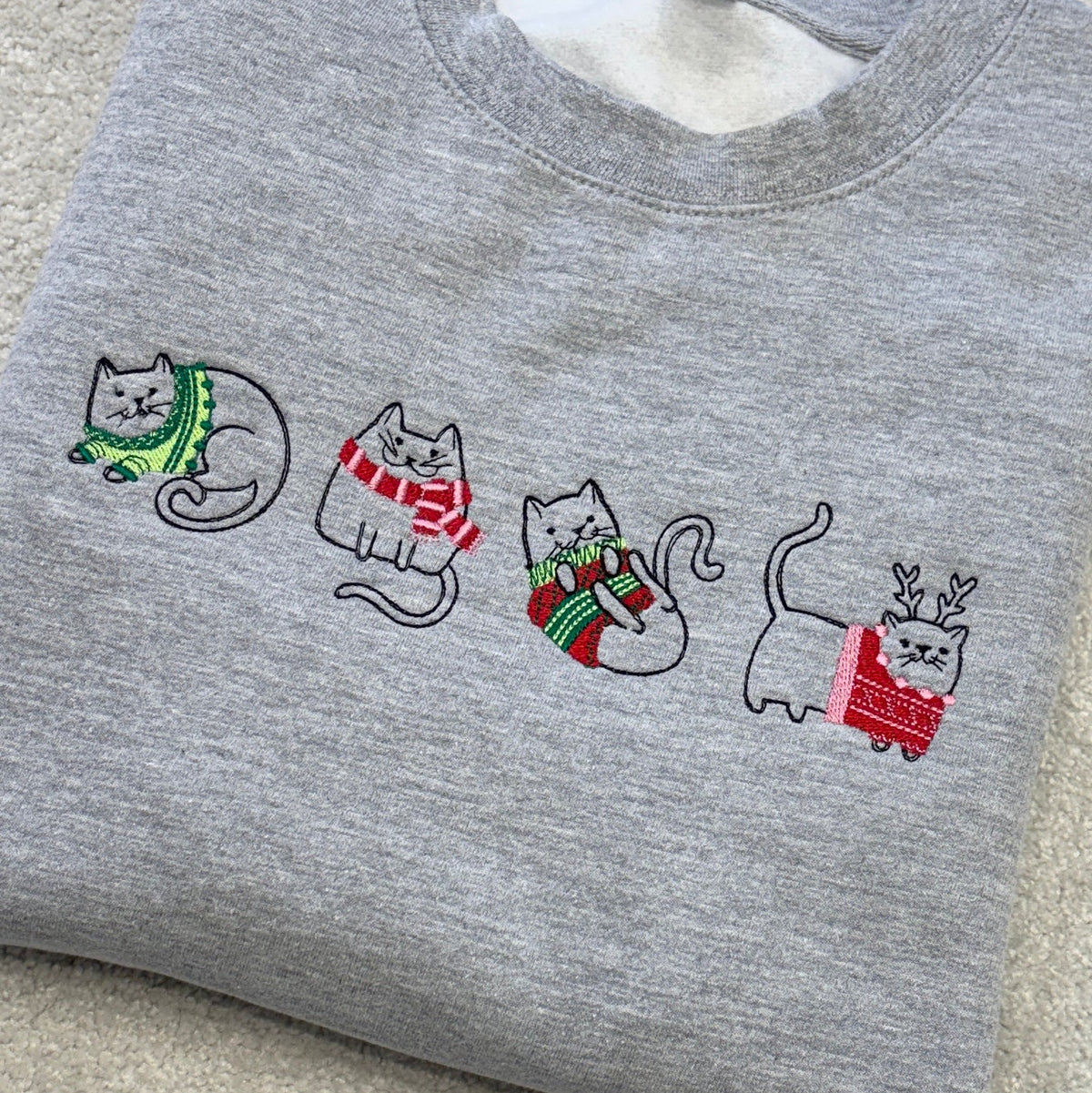 Four sketch style cats across the front of a heather grey sweatshirt, wearing christmas jumpers and scarves