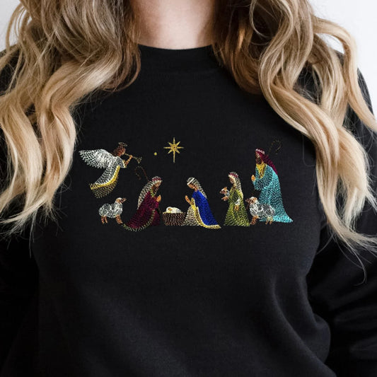 Black sweatshirt with embroidered nativity scene design worn by a person with blonde hair.