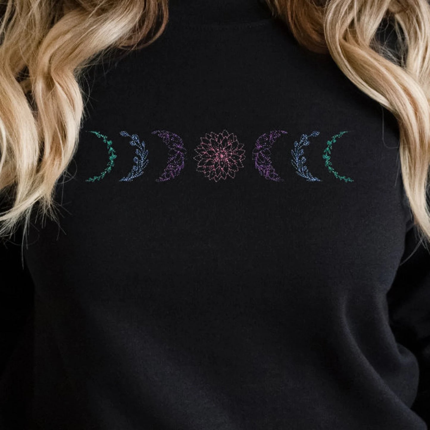 Black sweatshirt with embroidered design featuring moon phases, worn by a woman with blonde hair.