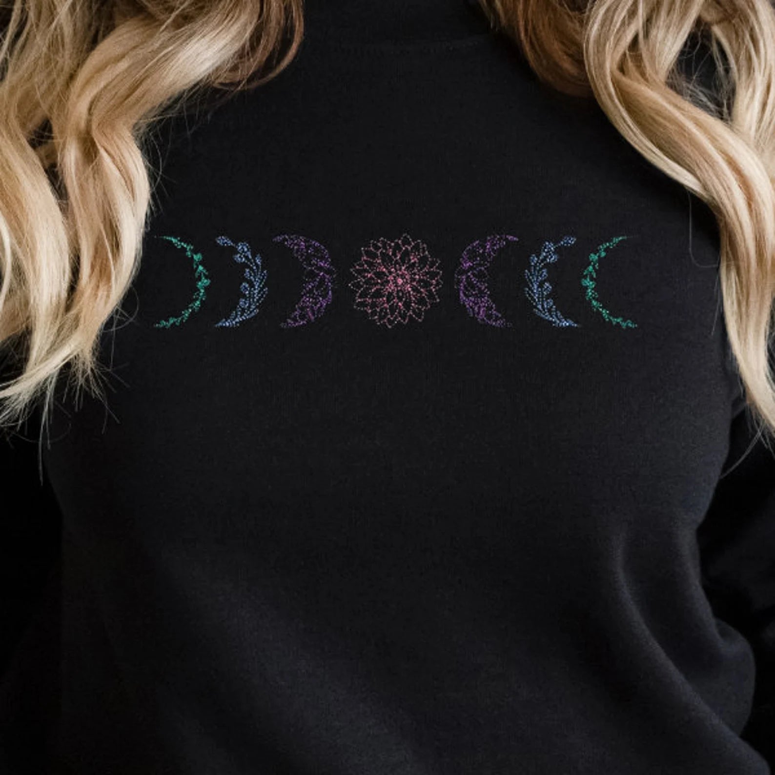 Black sweatshirt with embroidered design featuring moon phases, worn by a woman with blonde hair.