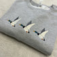 Grey sweatshirt with embroidered ducks flying through the air