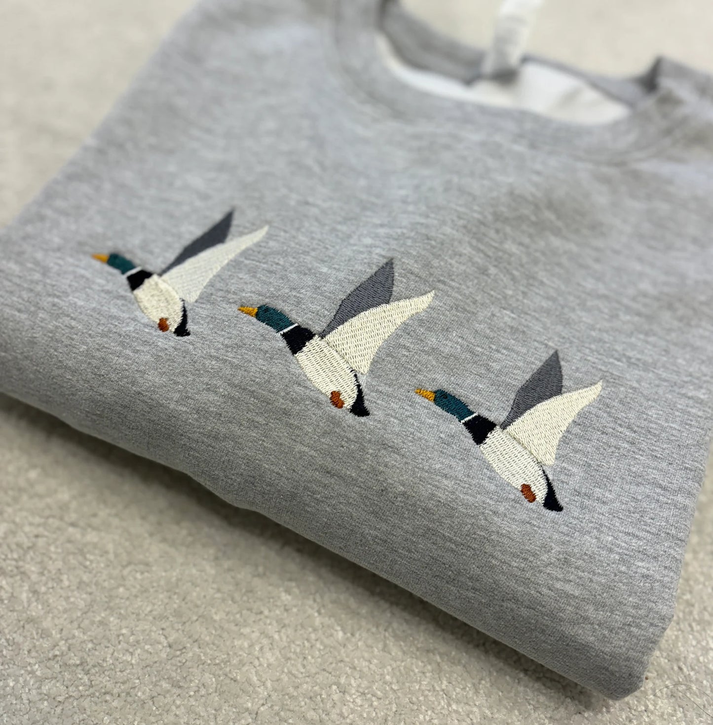 Grey sweatshirt with embroidered ducks flying through the air