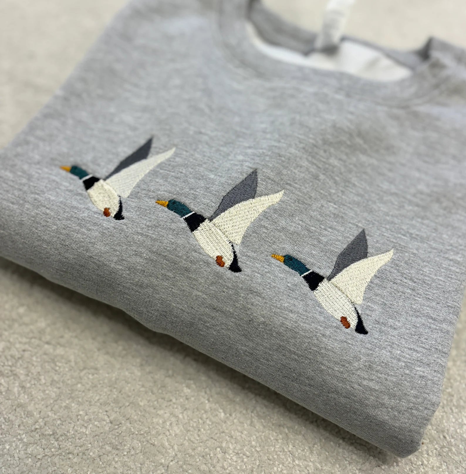 Grey sweatshirt with embroidered ducks flying through the air