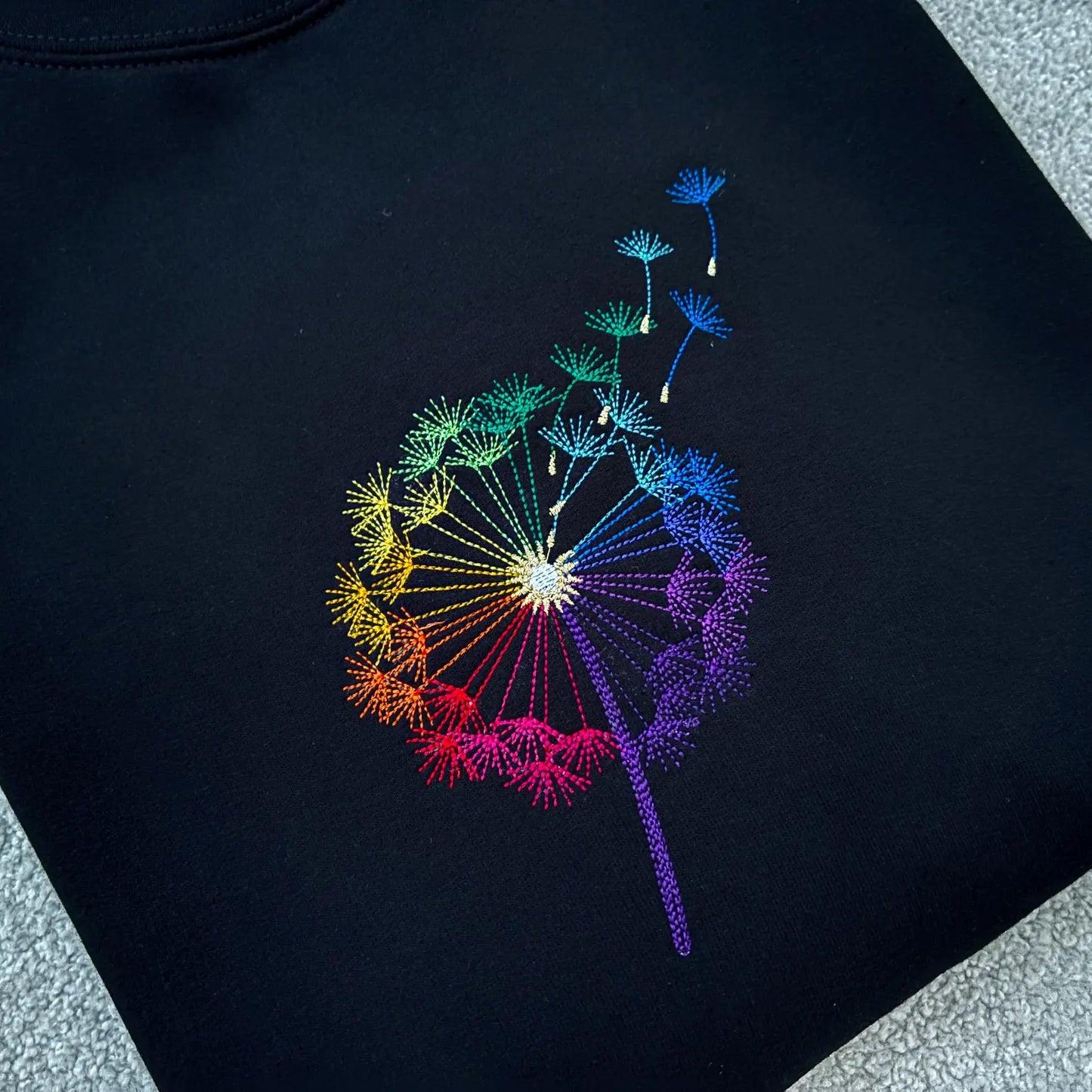 Black sweatshirt folded with a colourful embroidered dandelion clock design 