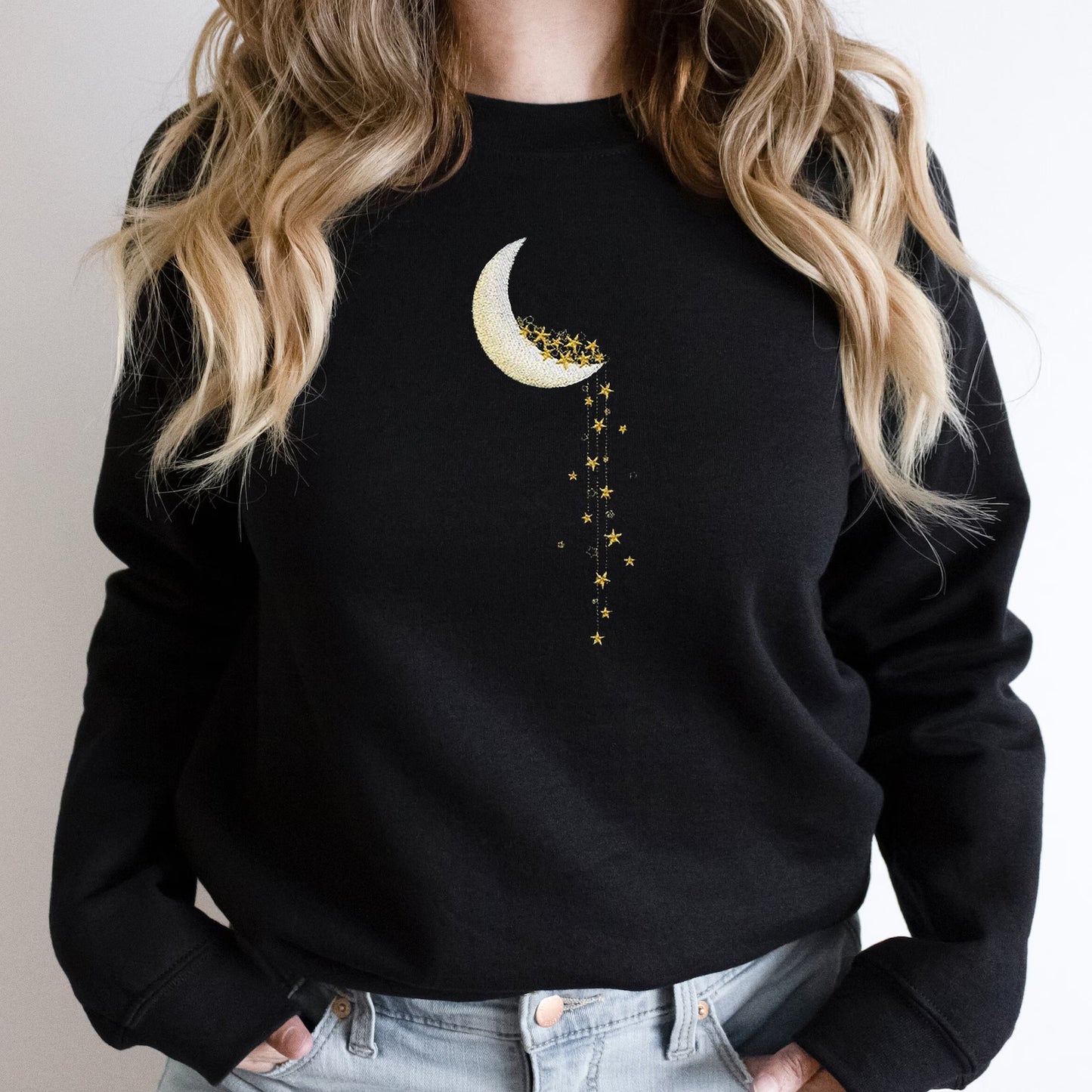 Black sweatshirt with a moon and star design worn by a person with blonde hair.