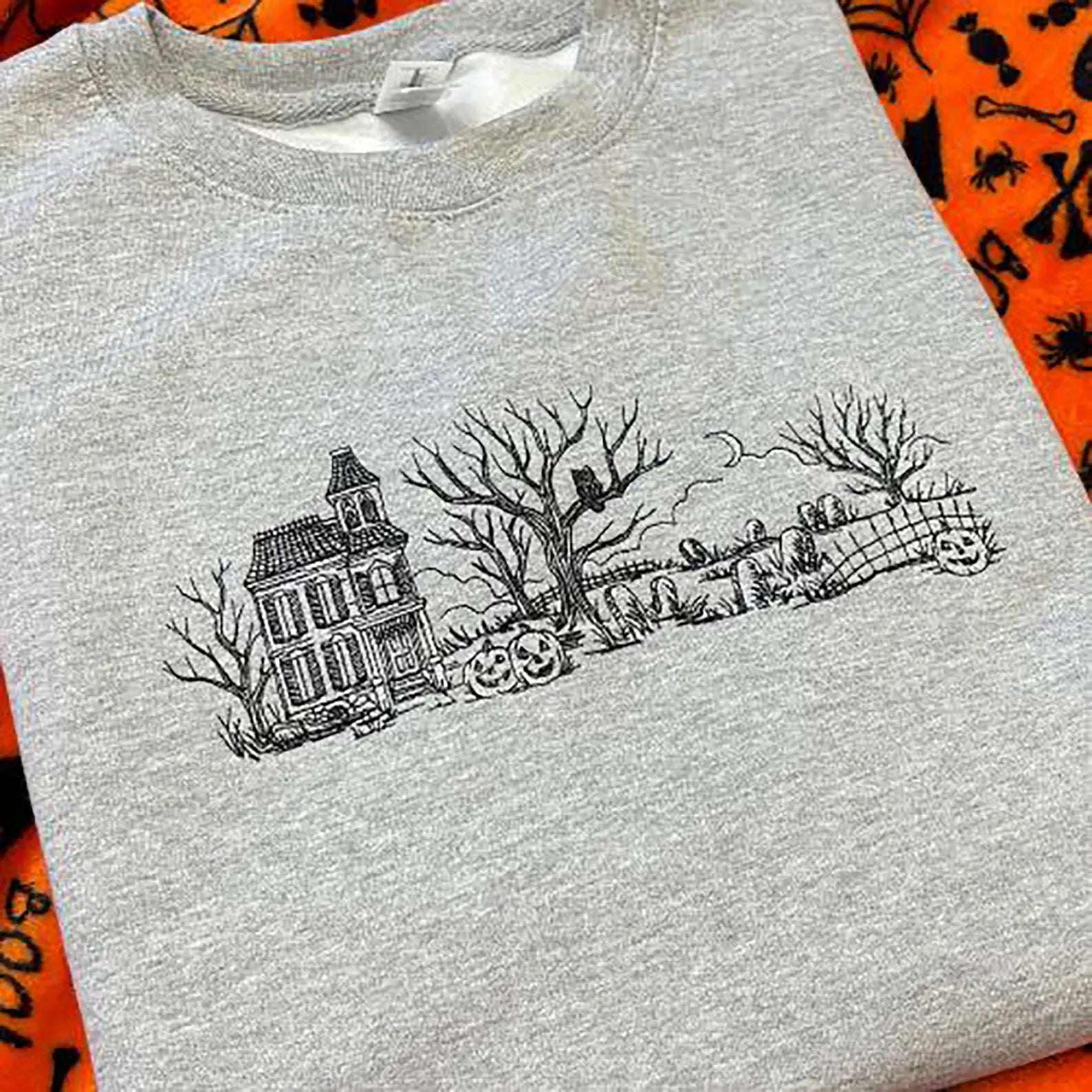 Grey sweatshirt with a black Halloween-themed embroidered design of a haunted house and graveyard.