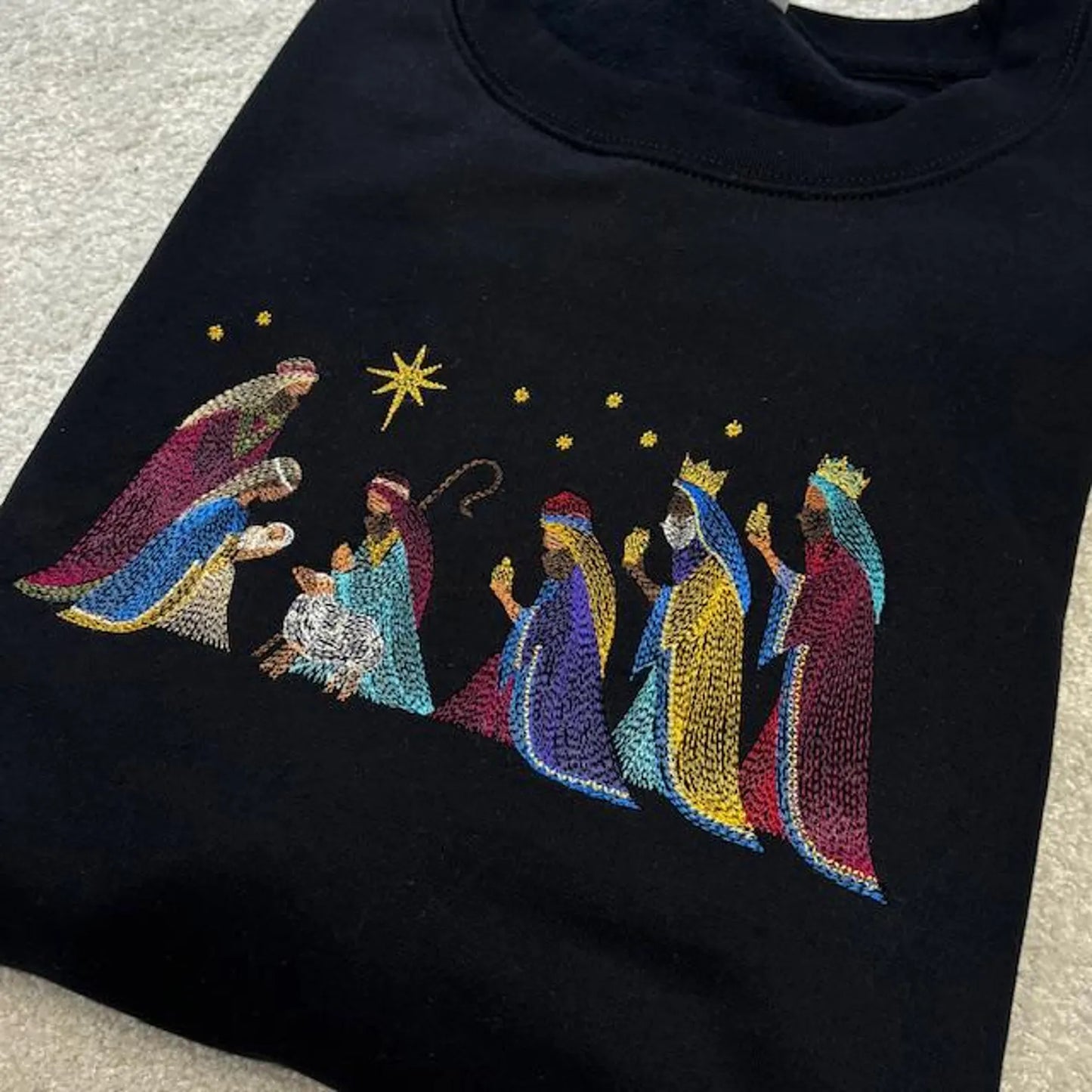 Black sweatshirt with embroidered nativity scene design.