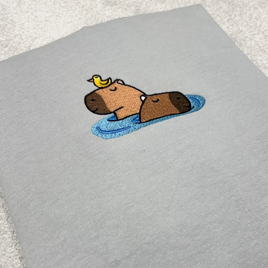 Embroidered design of a capybara and a bird on a grey fabric background