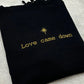 Black embroidered sweatshirt with gold text 'Love came down' and star