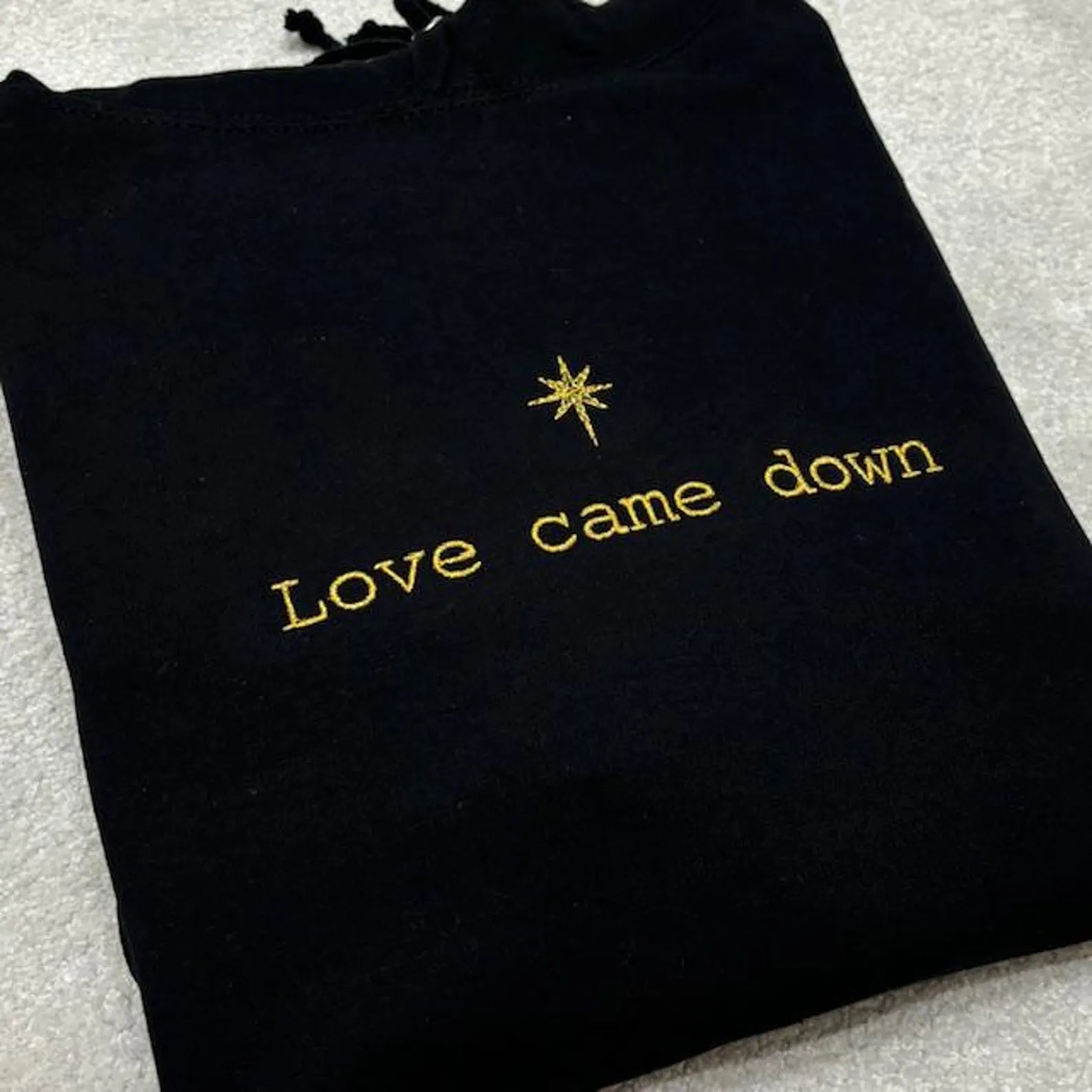 Black embroidered sweatshirt with gold text 'Love came down' and star