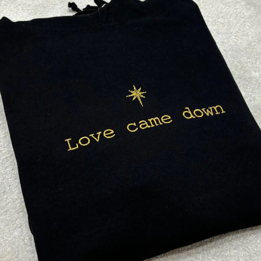 Black embroidered sweatshirt with gold text 'Love came down' and star