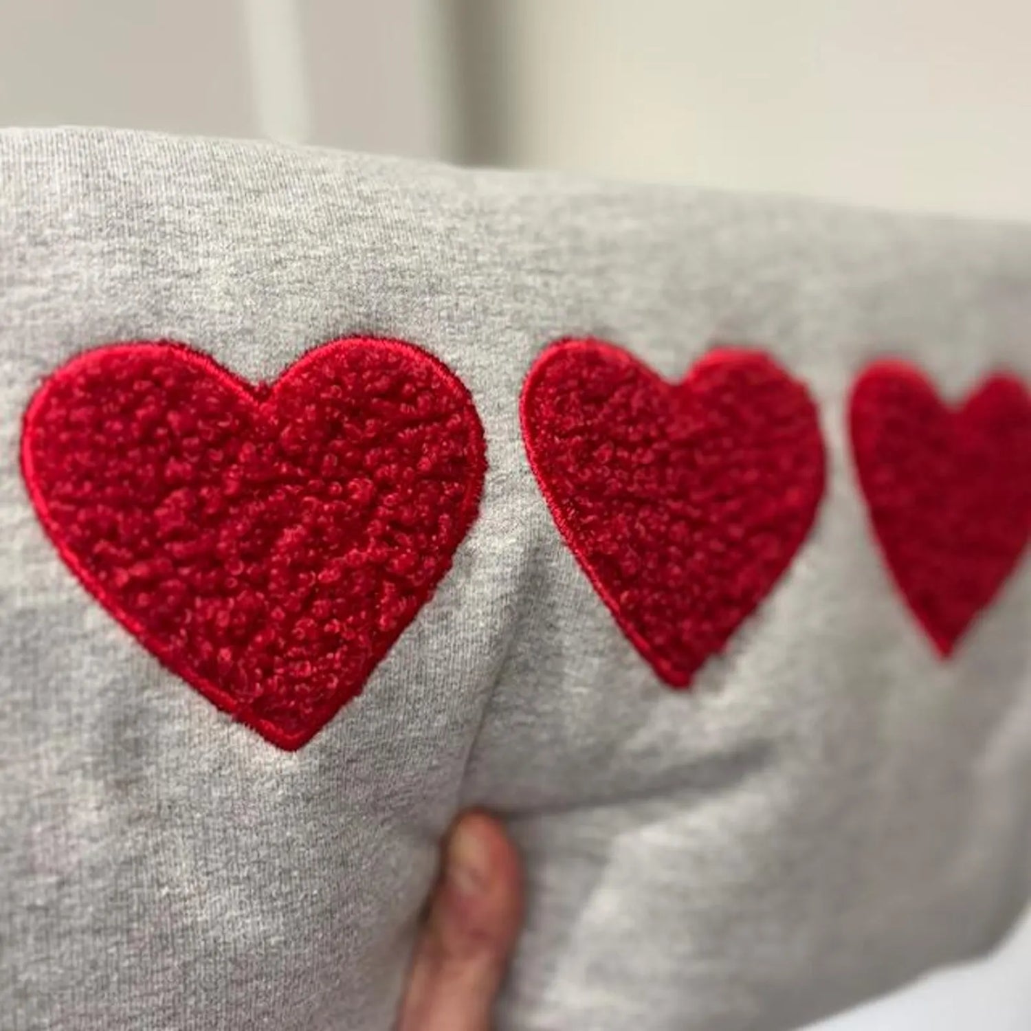 A trio of red boucle hearts appliqued onto a grey sweatshirt. Held by the owner.