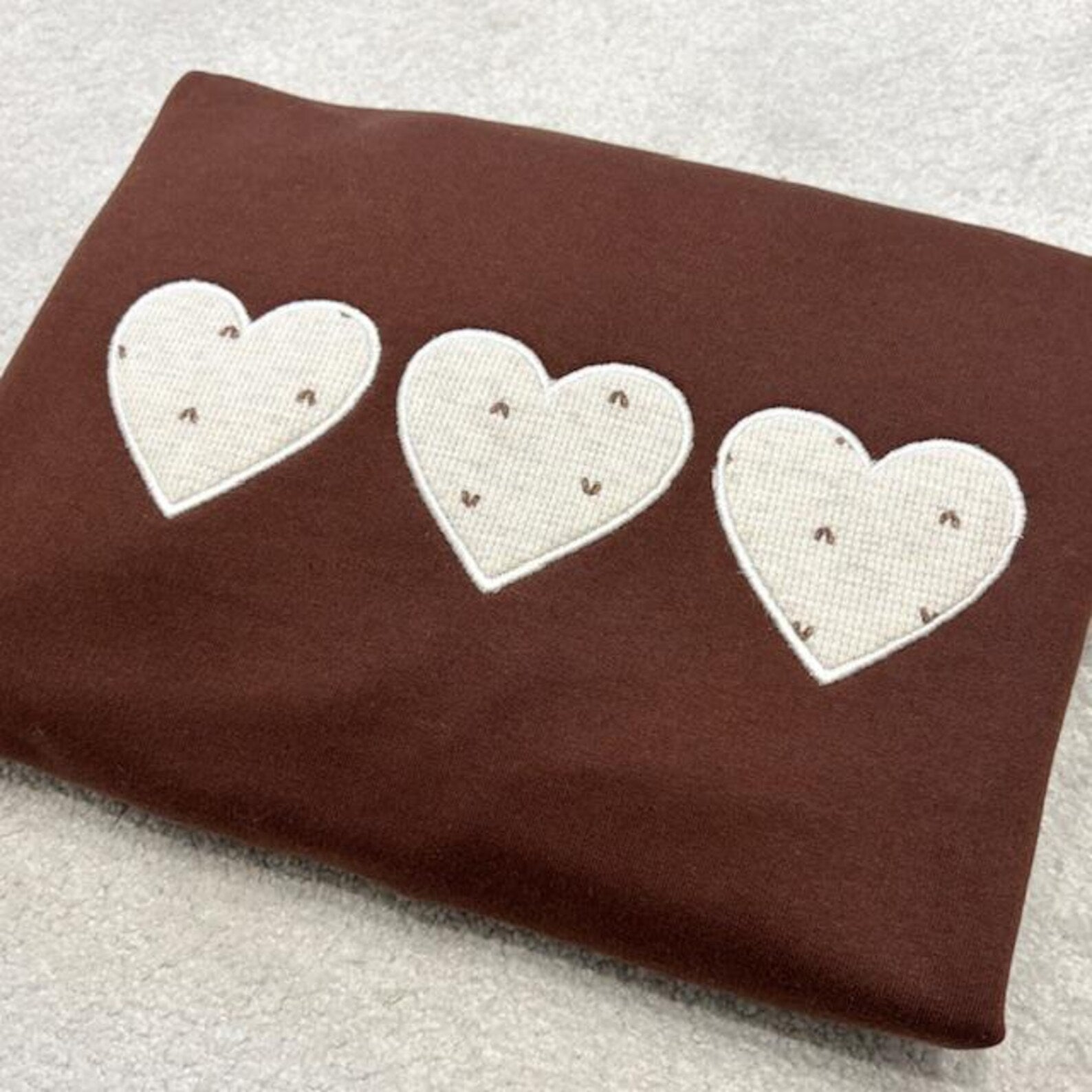 Folded brown sweatshirt with three applique hearts made using baby grows. Placed on a white background