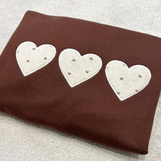 Folded brown sweatshirt with three applique hearts made using baby grows. Placed on a white background