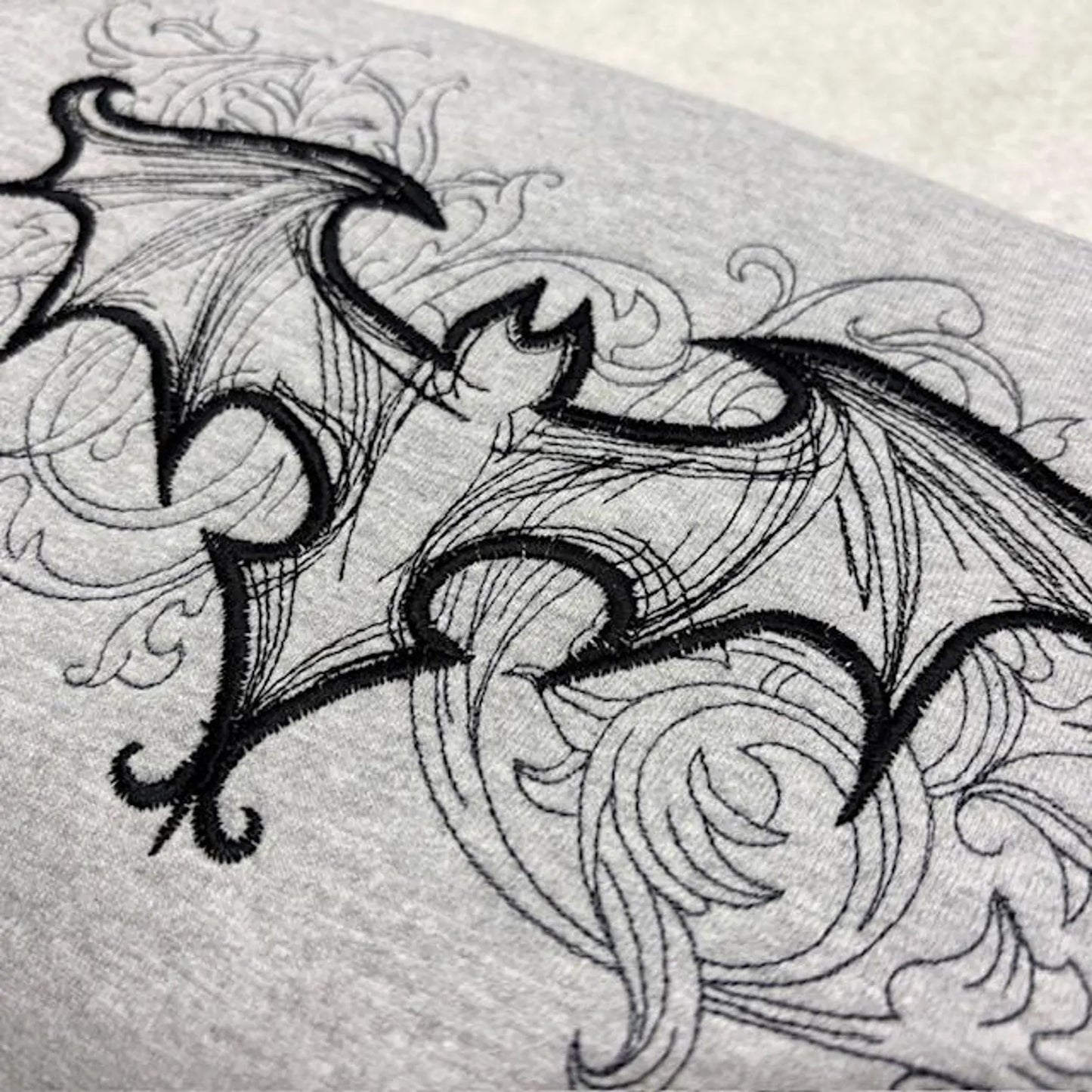 Detailed black line drawing of a gothic bat on a grey sweatshirt