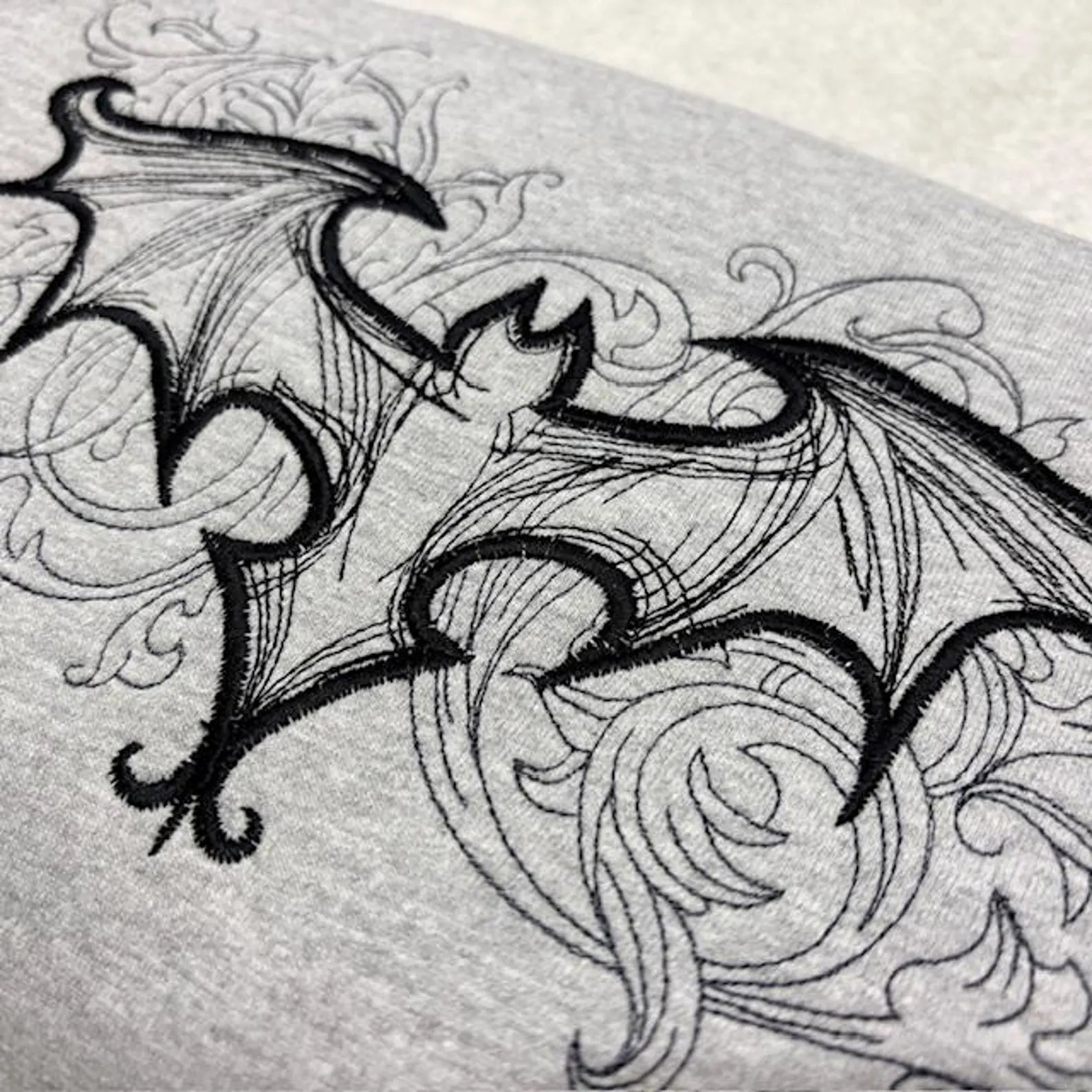 Detailed black line drawing of a gothic bat on a grey sweatshirt