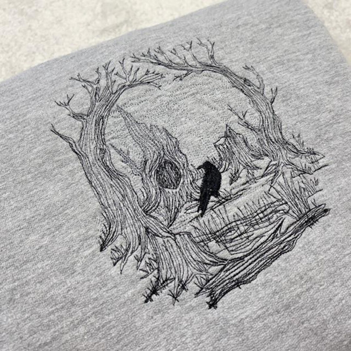 Embroidered sketch style of a skull on a grey sweatshirt