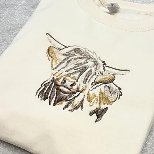 Embroidered design of a highland cow on a cream sweatshirt.